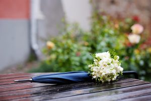 An umbrella folded up near a wedding bouquet, showing that a rainy wedding is taking place.